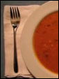 Тарелка аппетитного мясного, горячего борща, украшенного зеленью и вилка с ножем.
