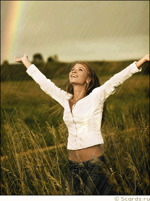 Девушка жизнераадостно стоит под дождем подняв руки к небу посреди чистого поля, позади виднеется радуга.