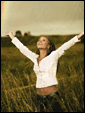 Девушка жизнераадостно стоит под дождем подняв руки к небу посреди чистого поля, позади виднеется радуга.