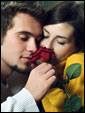 Парень и девушка, прижавшись друг ко другу, вдыхают аромат алой розы.