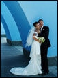 Молодожены: парень и девушка стоят прижавшись друг ко другу около синей арки.