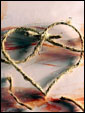 Упаковочная нитка завязана в форме сердечка на фоне разноцветного холста.