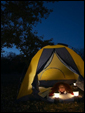 Девушка в палатке при свете ночных фонарей поздравляет получателя открытки с приходом лета.